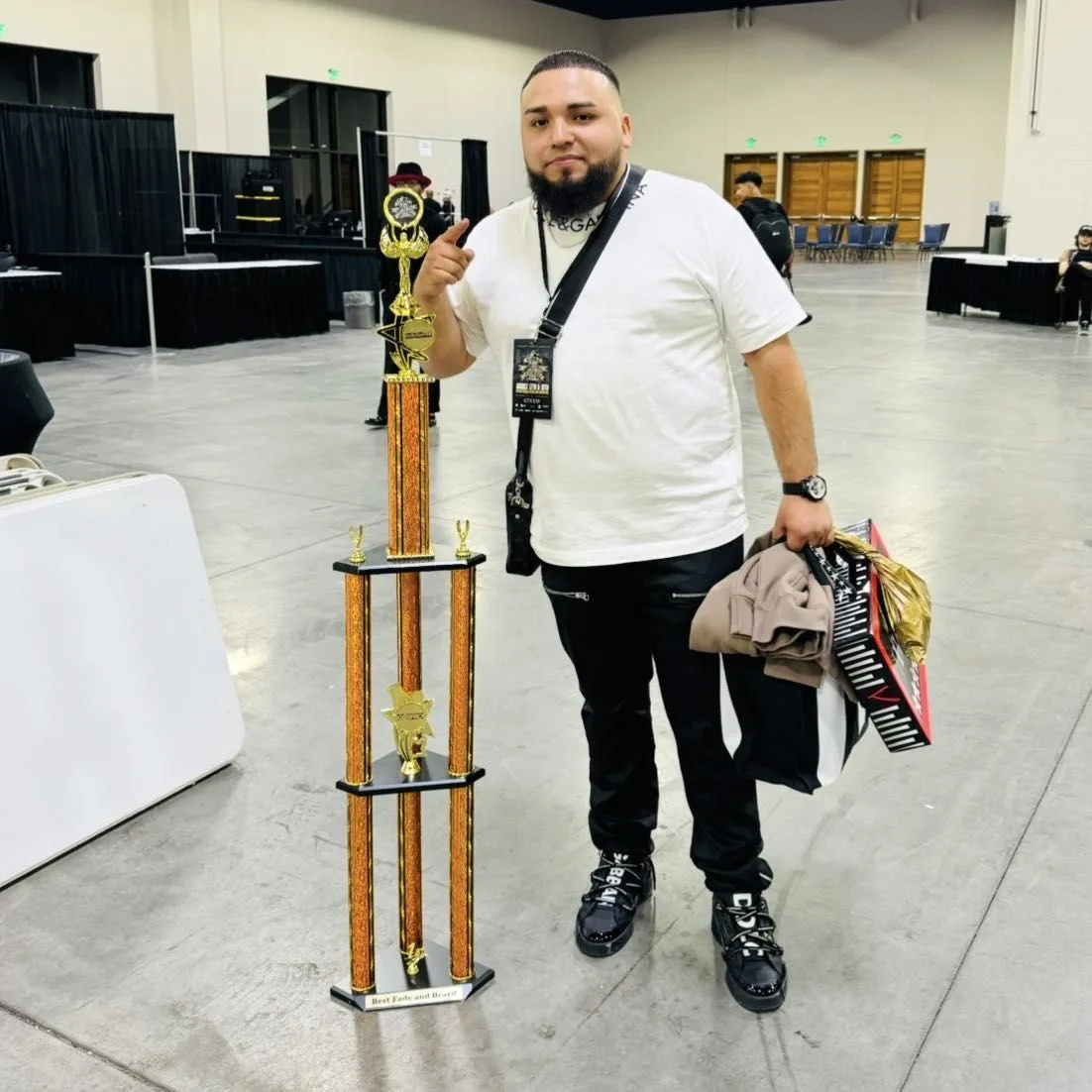Barber Chivero standing with a tall competition trophy at a barber event